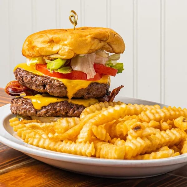 A double bacon cheeseburger with lettuce, tomato, and crinkle-cut fries on a white plate.
