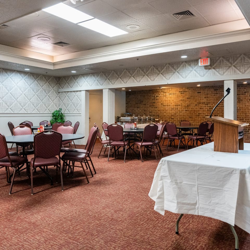 Empty banquet room at Barnes Restaurant with tables, chairs, a buffet, and a podium.