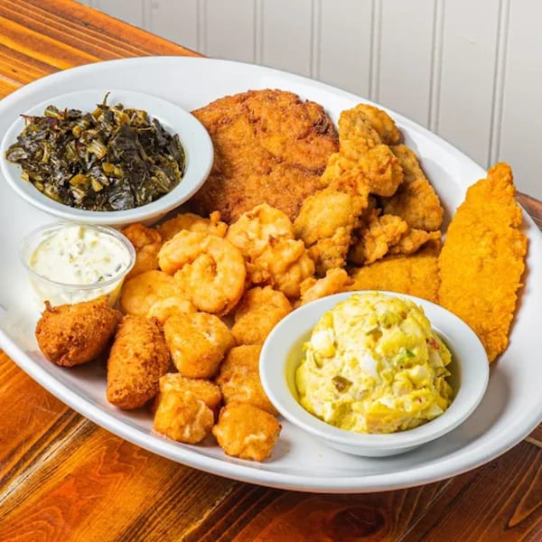 A large platter of fried seafood, hush puppies, collard greens, potato salad, and tartar sauce.