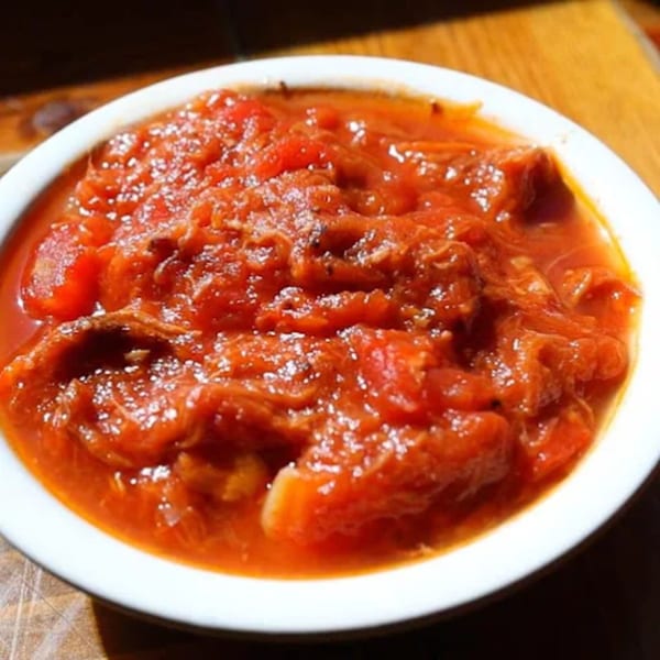 A white bowl filled with chunky, bright red tomato relish or sauce, possibly for BBQ.